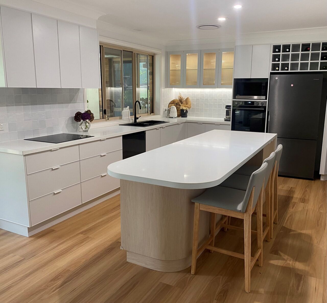 A white kitchen with a curved stone island